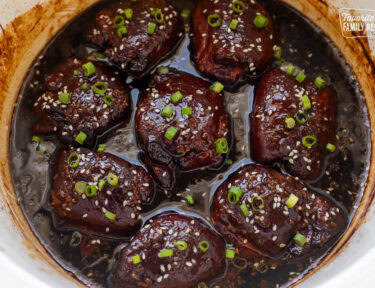 Crockpot with cooked Hawaiian chicken thighs, garnished with green onion and sesame seeds.