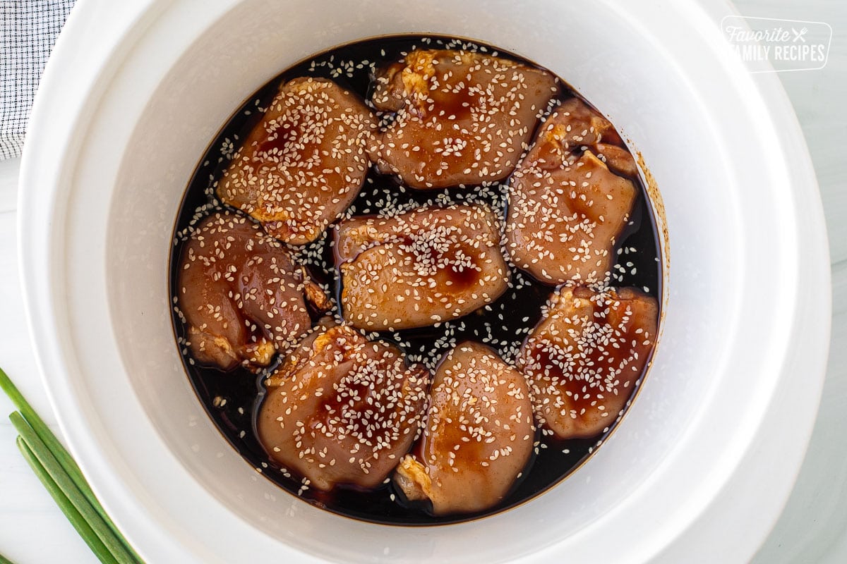 Crockpot with uncooked chicken thighs, Mr. Yoshida sauce and sesame seeds.