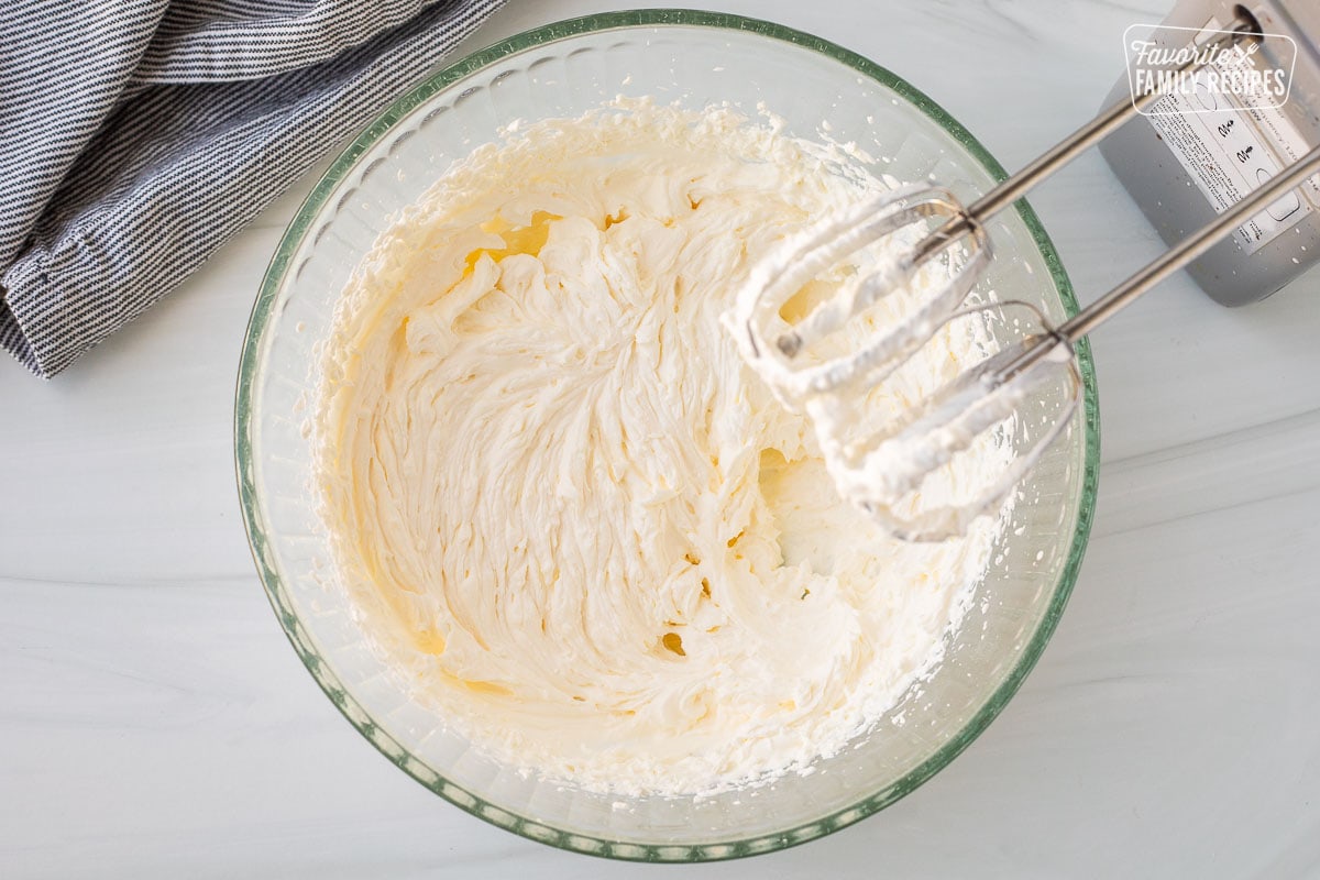 Mixing bowl with whipped heavy cream and electric mixer.