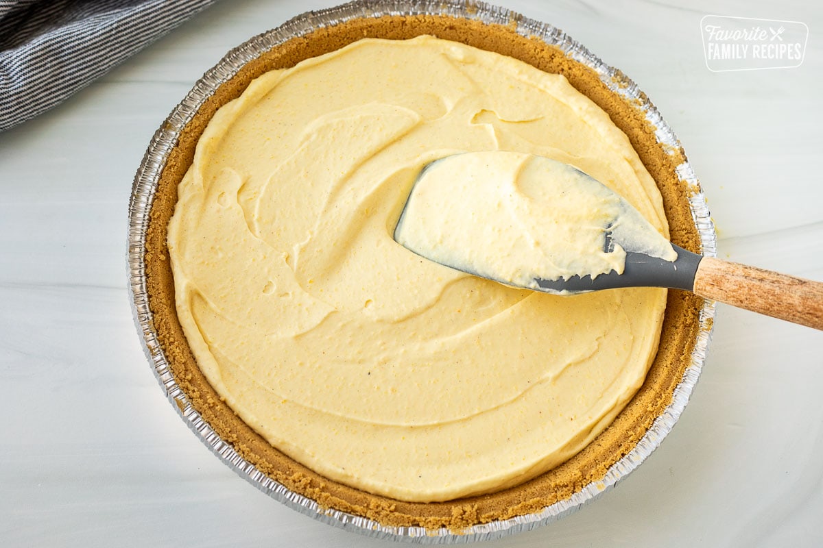 Spatula spreading egg nog pie filling into graham cracker crust.