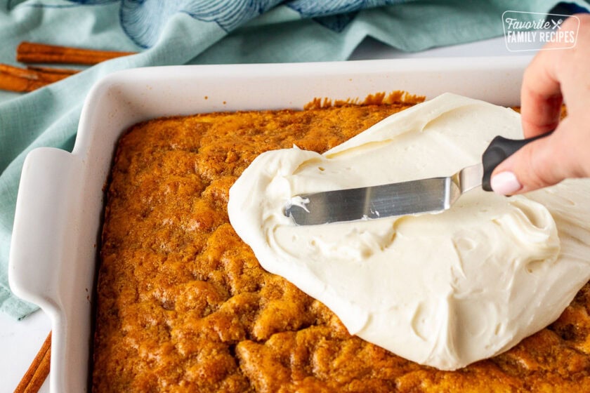 Spreading frosting on top of cinnamon roll cake.