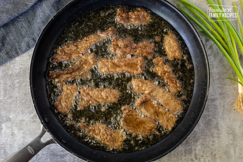 Skillet of oil frying sliced steak.