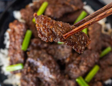 Chopsticks holding up a slice of Mongolian beef.