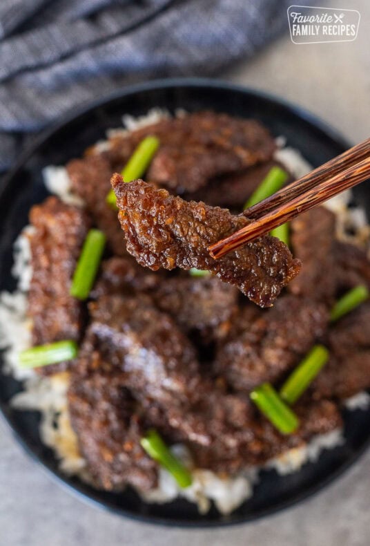 Chopsticks holding up a slice of Mongolian beef.