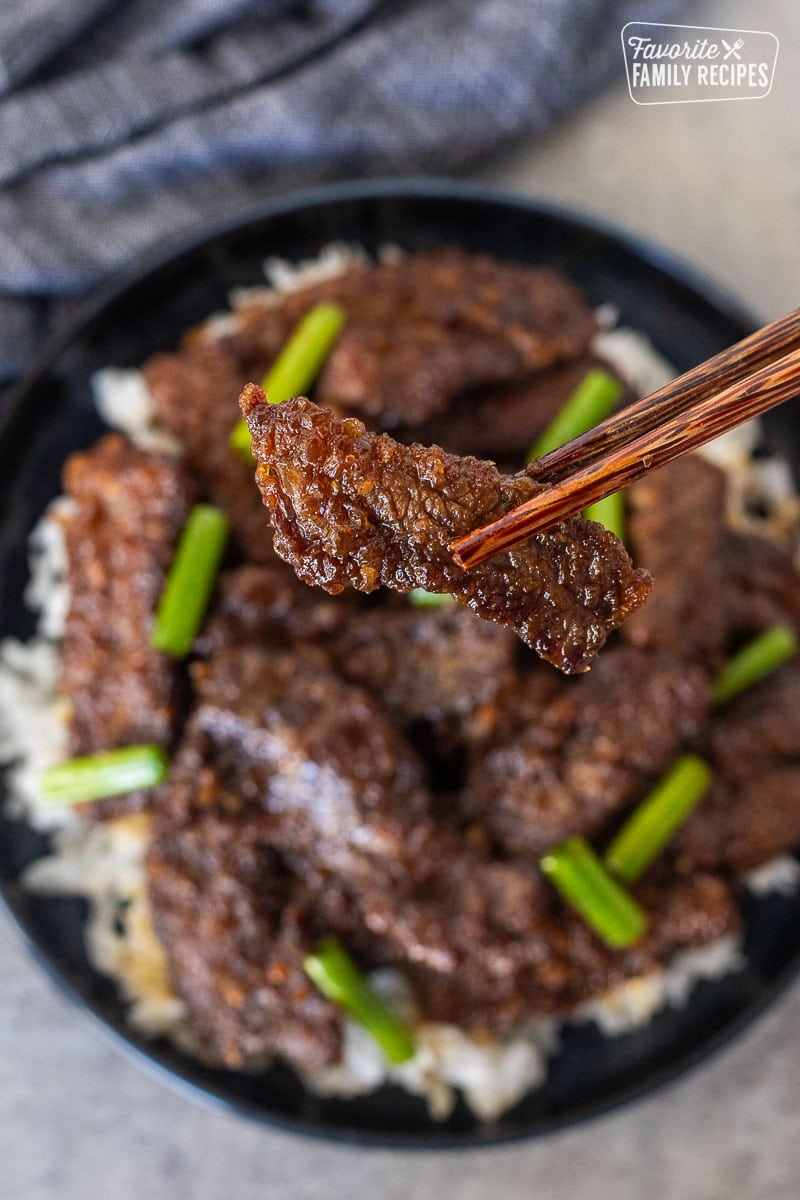 Chopsticks holding up a slice of Mongolian beef.