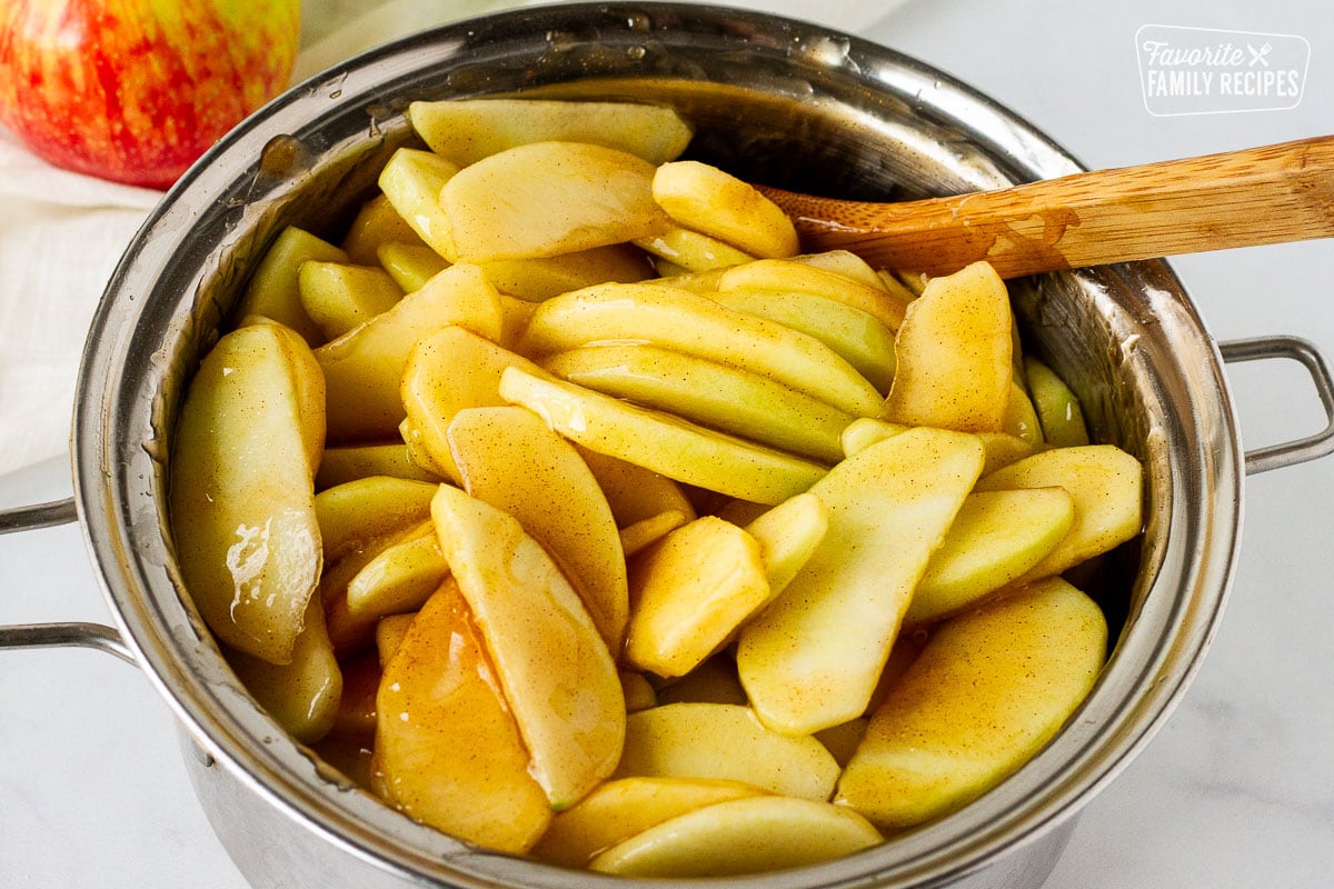 Saucepan of sliced apples in Homemade Apple Pie filling with wooden spoon.