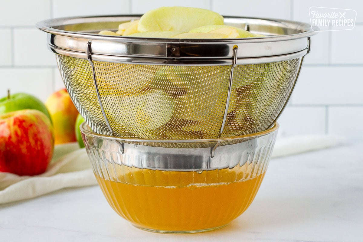 Sliced apples in a colander draining into a bowl for pie filling.