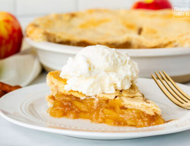 Side view of Homemade Apple Pie topped with a large scoop of vanilla ice cream. Whole pie in the background.