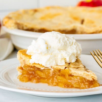 Side view of Homemade Apple Pie topped with a large scoop of vanilla ice cream. Whole pie in the background.