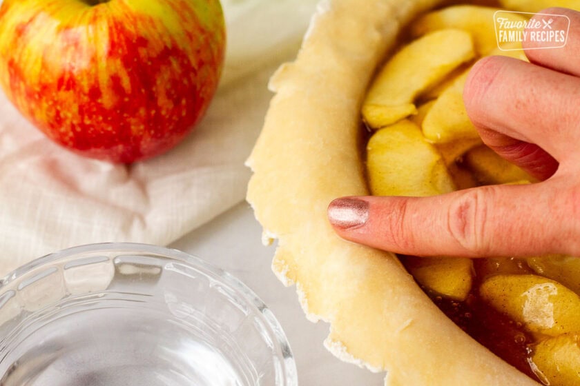 Finger with water rubbing around Apple Pie shell.