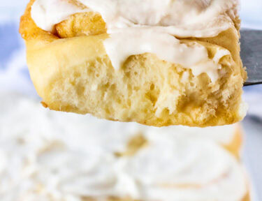 Cinnamon roll held up on a spatula with frosting.