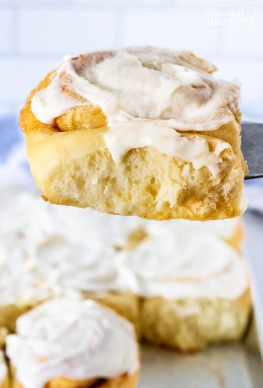 Cinnamon roll held up on a spatula with frosting.