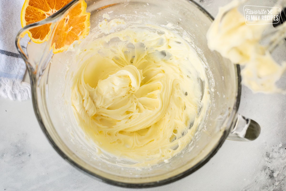 Glass mixing bowl with orange frosting for homemade orange rolls.