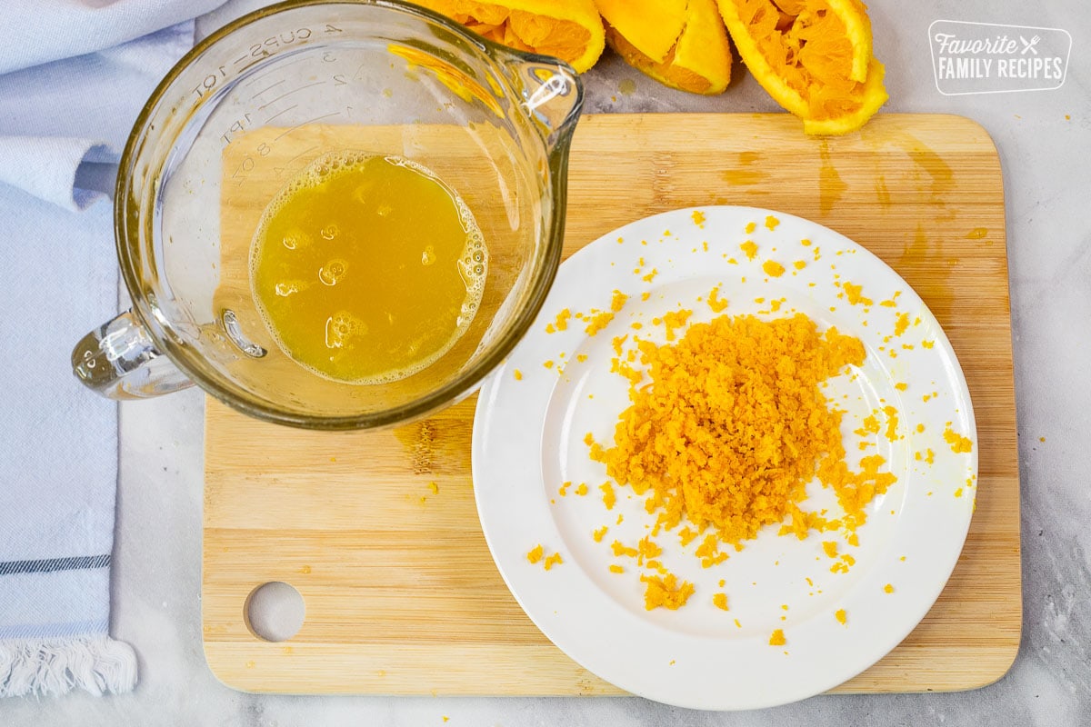 Cutting board with orange zest on a plate and orange juice in a bowl.