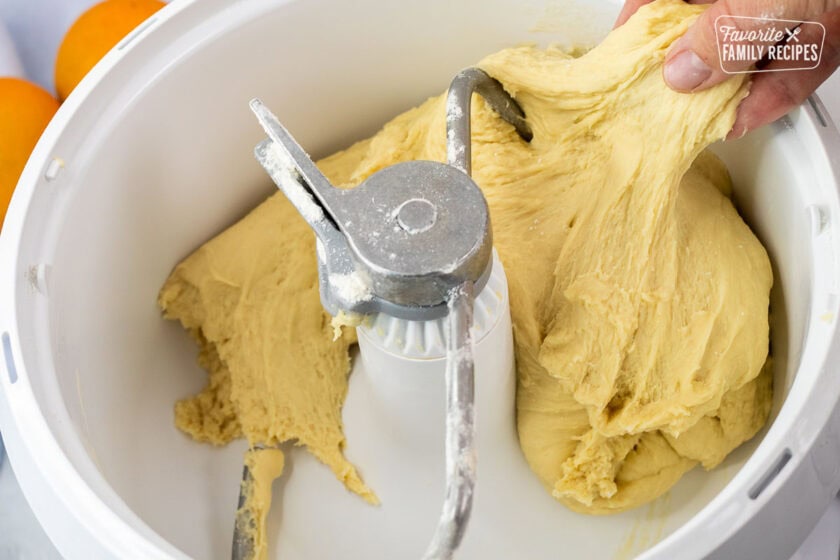 Hand pulling the homemade orange roll dough out of the mixing bowl.