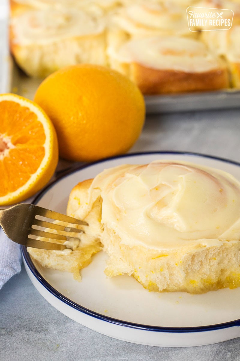 Homemade orange roll frosted on a plate with a fork pulling it apart. Most