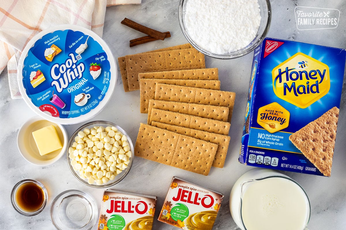 Ingredients to make Pumpkin Eclair Cake including graham crackers, powdered sugar, Cool Whip, white chocolate chips, butter, vanilla, water, cream and pumpkin spice pudding.