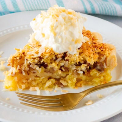 Slice of Island Pecan Pie on a plate topped with whipped cream and toasted coconut.