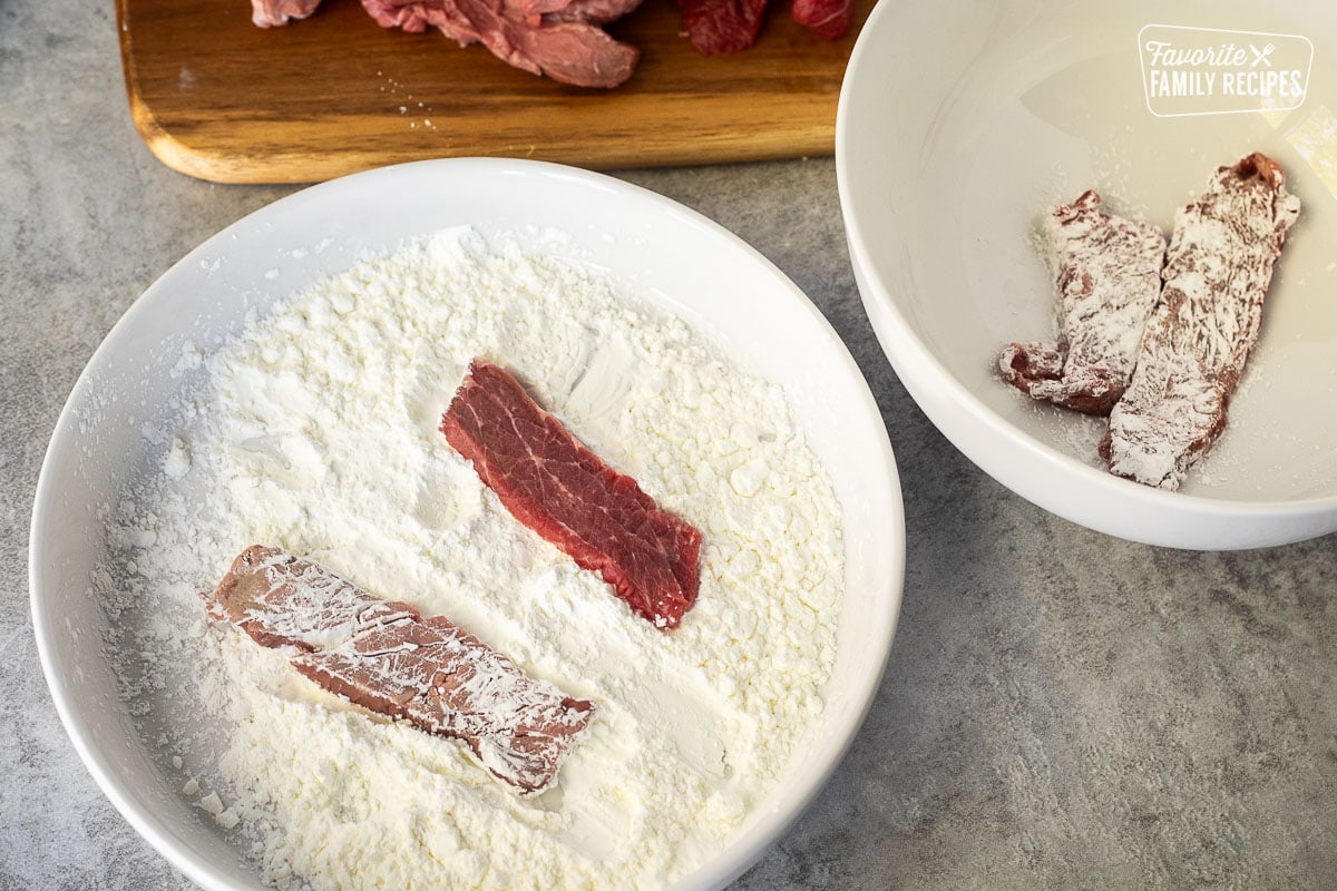 Sliced flank steak dipping into a shallow bowl of cornstarch.