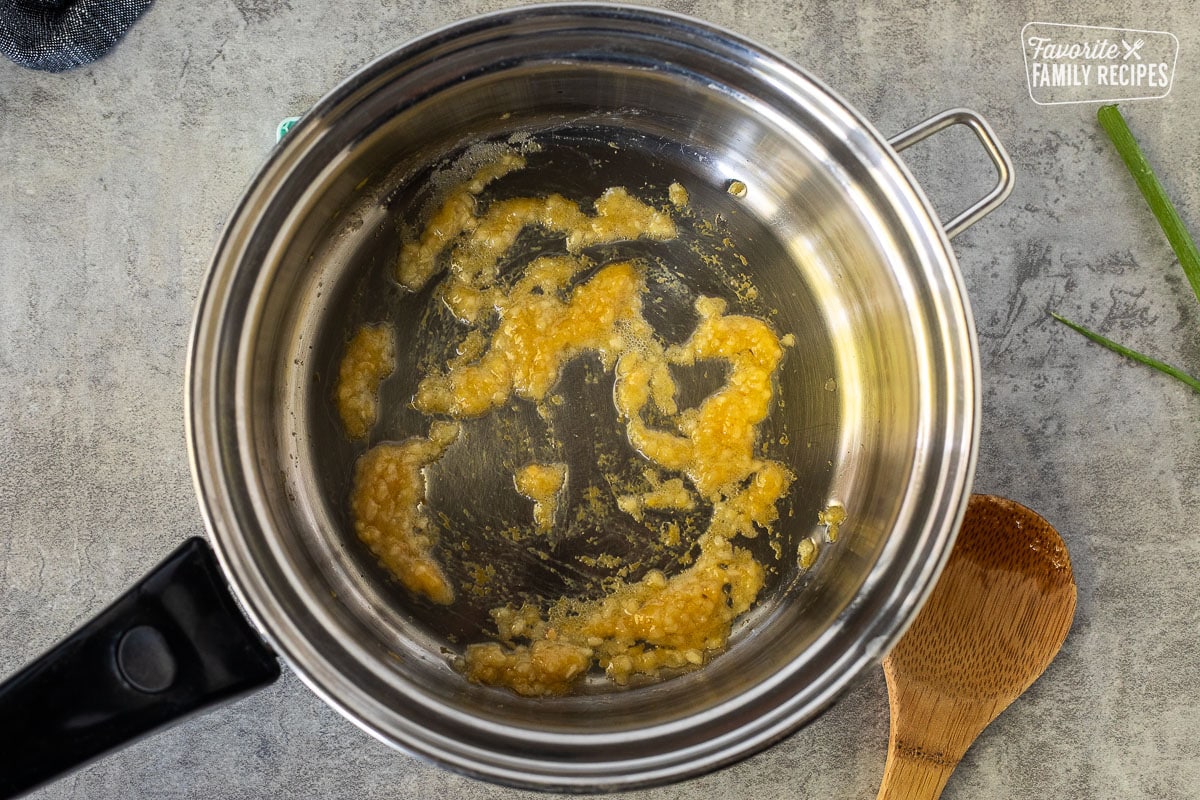 Saucepan with oil, garlic, and ginger. Wooden spoon on the side.