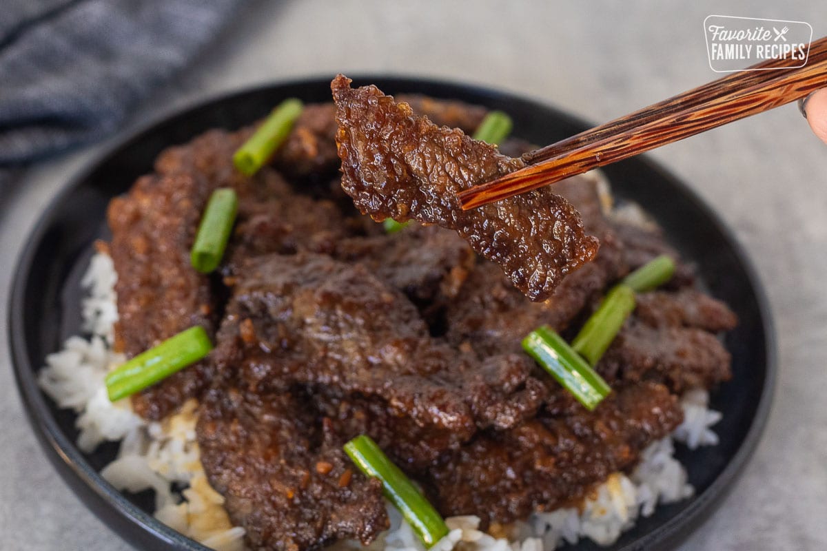 Chopsticks holding up a slice of Mongolian beef.