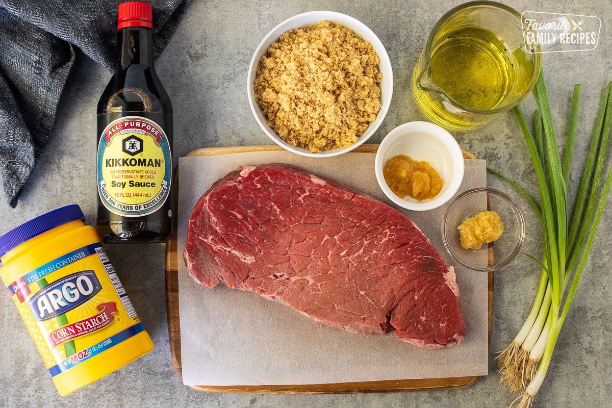 Ingredients to make Mongolian beef, including flank steak, garlic, ginger, oil, brown sugar, soy sauce, cornstarch, and fresh green onion.