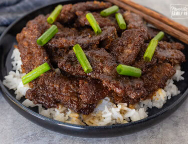 Mongolian beef with green onion over rice on a plate.