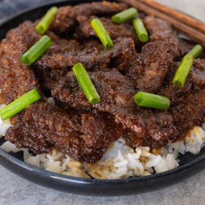 Mongolian beef with green onion over rice on a plate.