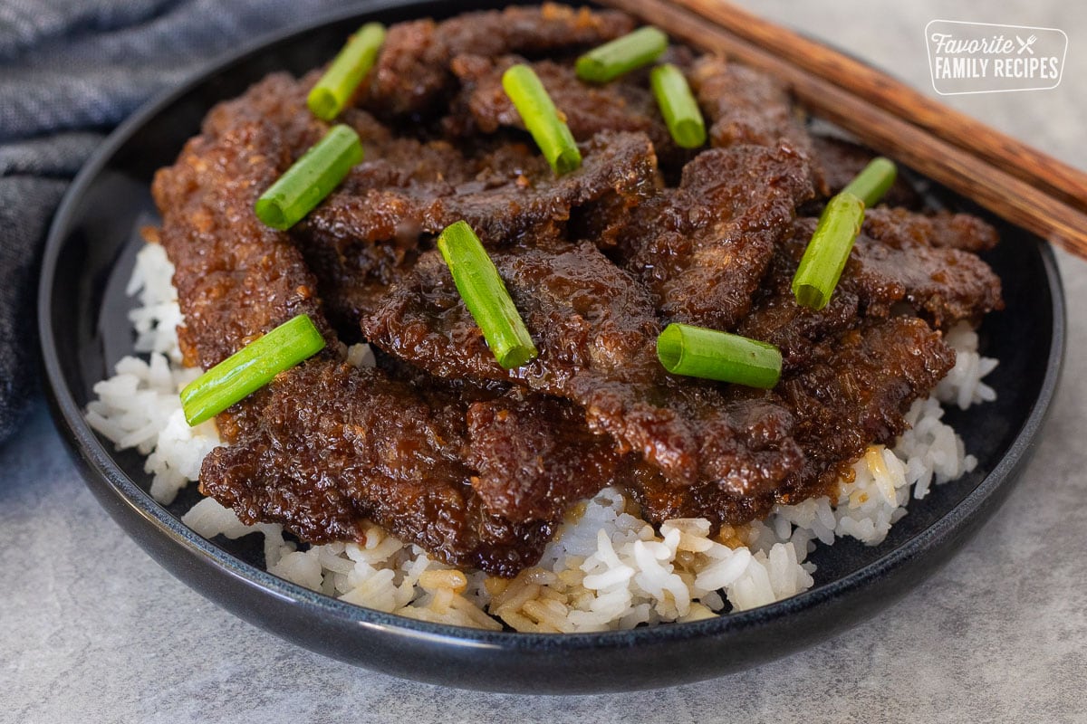 Mongolian beef with green onion over rice on a plate.