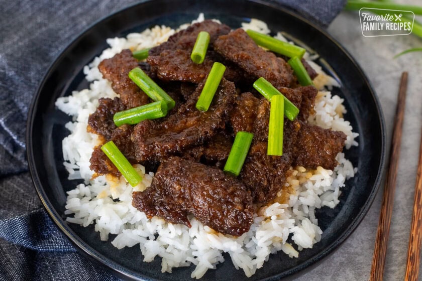 Mongolian beef with green onion over rice on a plate.