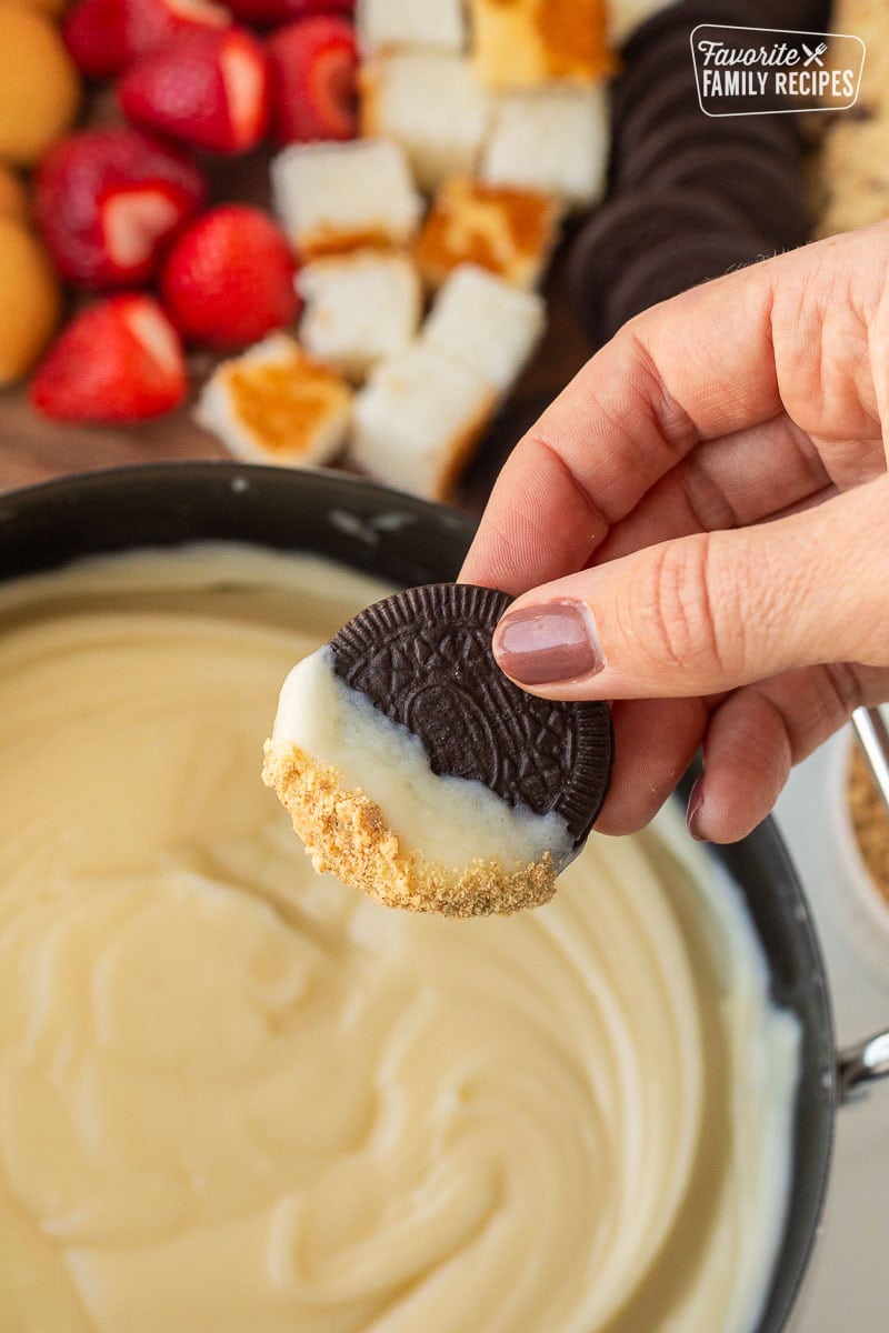 Hand holding an Oreo cookie dipped in Cheesecake Fondue.