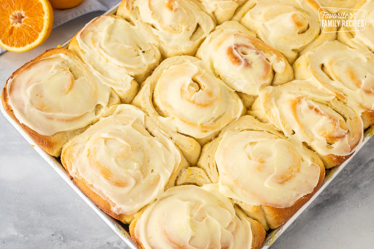 Frosted homemade orange rolls in a baking pan.