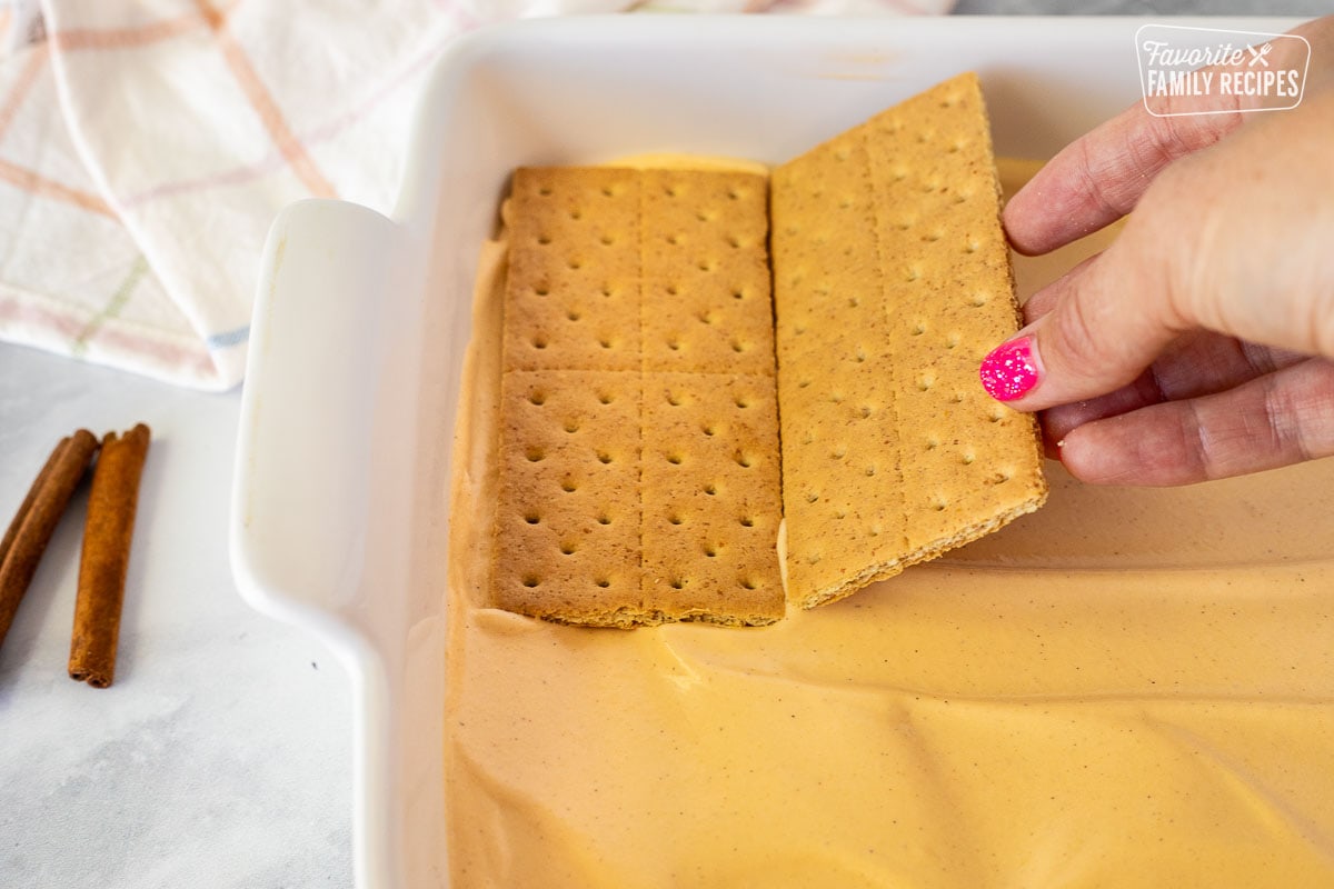 Layering graham crackers over pumpkin pudding for Pumpkin Eclair Cake.