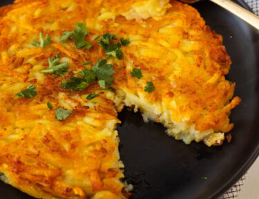 Rosti on a plate garnished with parsley and a cut out with a fork.