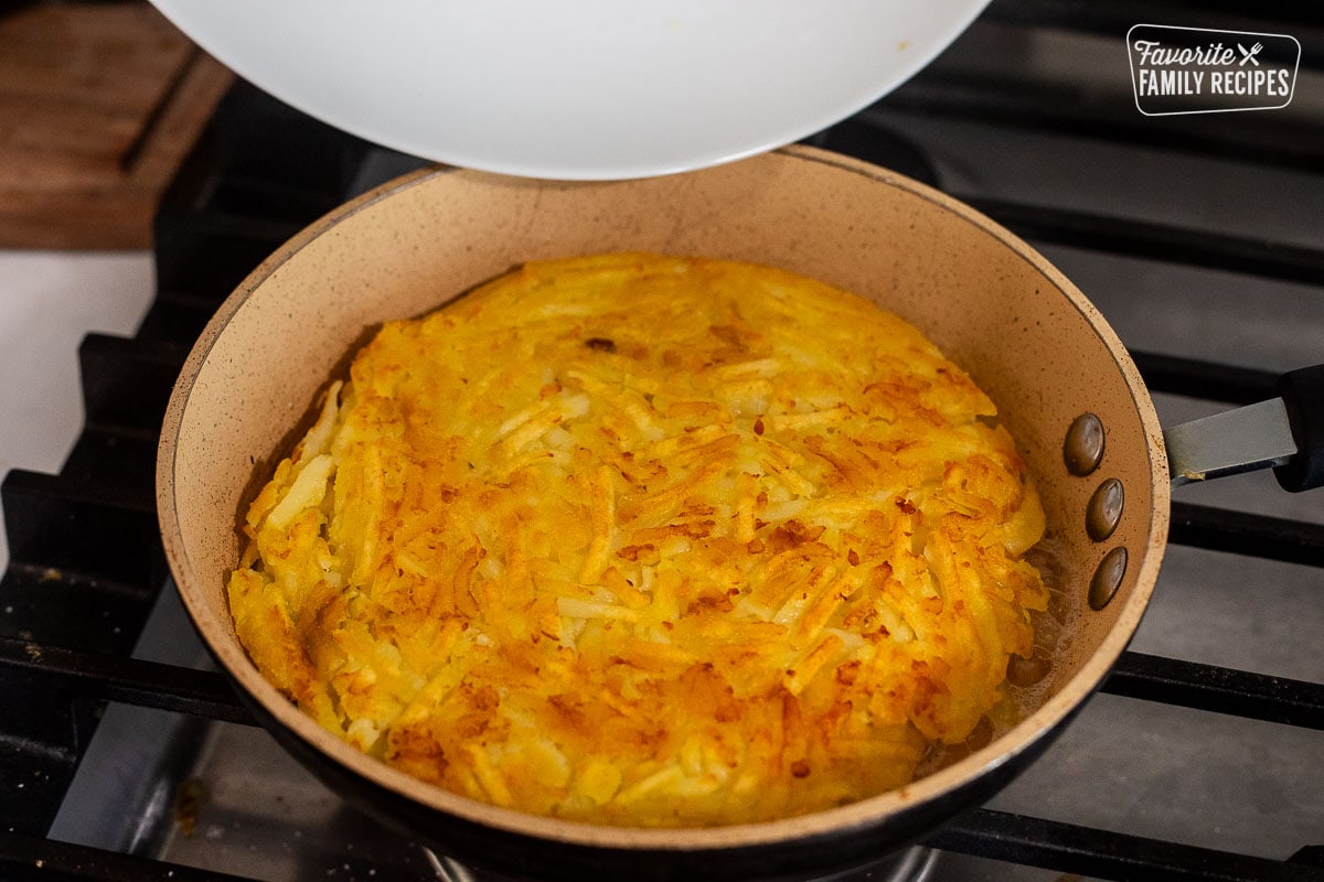 Flipped Rosti in a skillet with plate hovering above.