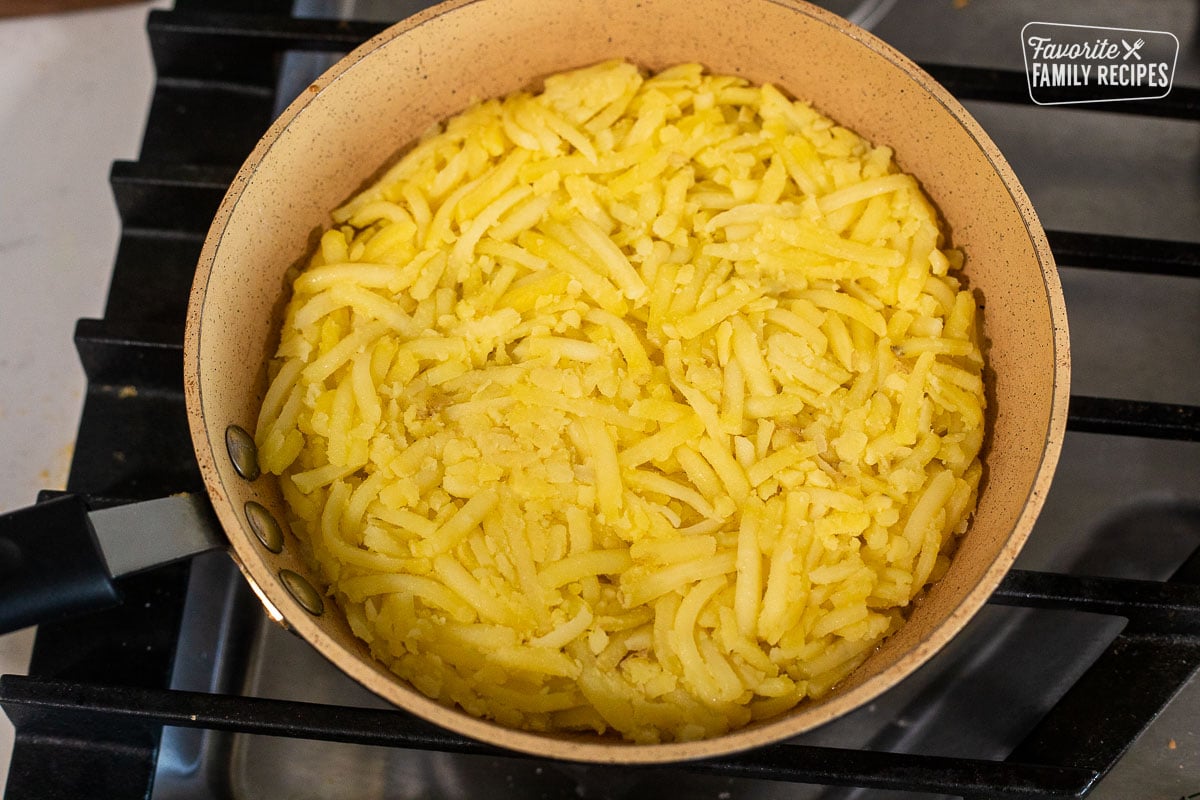 Skillet with shredded potatoes pressed in a circle shape.