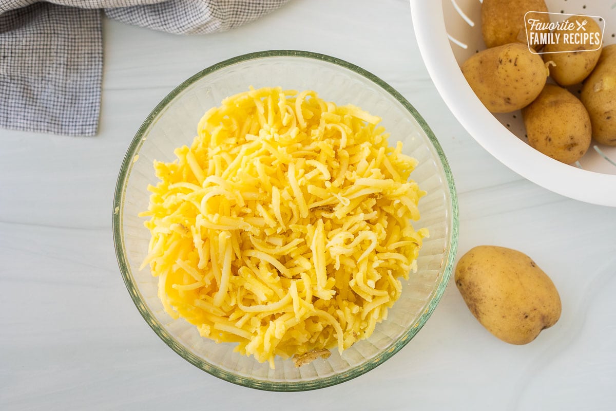 Shredded potatoes in a bowl next to colander of potatoes.