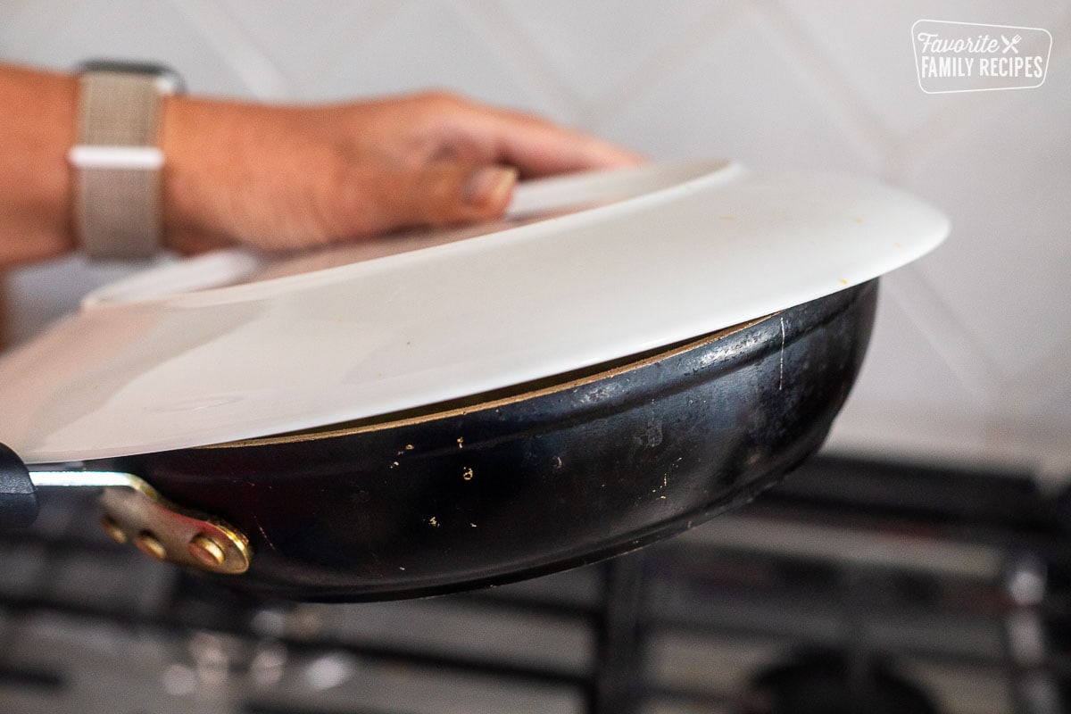 Placing a plate on top of skillet.