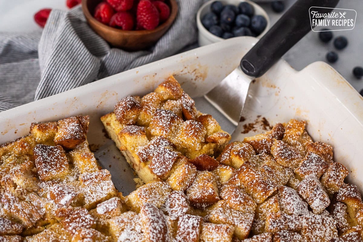 Spatula under a slice of brioche French toast casserole in a baking dish.