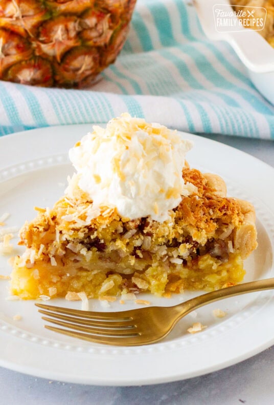 Slice of Island Pecan Pie on a plate topped with a coconut cream and toasted coconut. Fork resting on the plate.