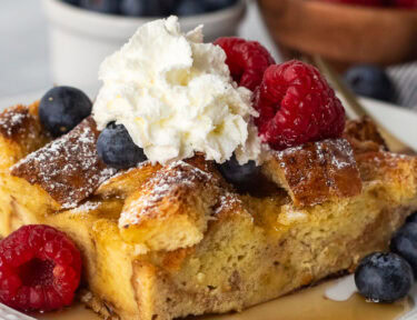 Plate with brioche French toast casserole, fresh blueberries, and raspberries and syrup.