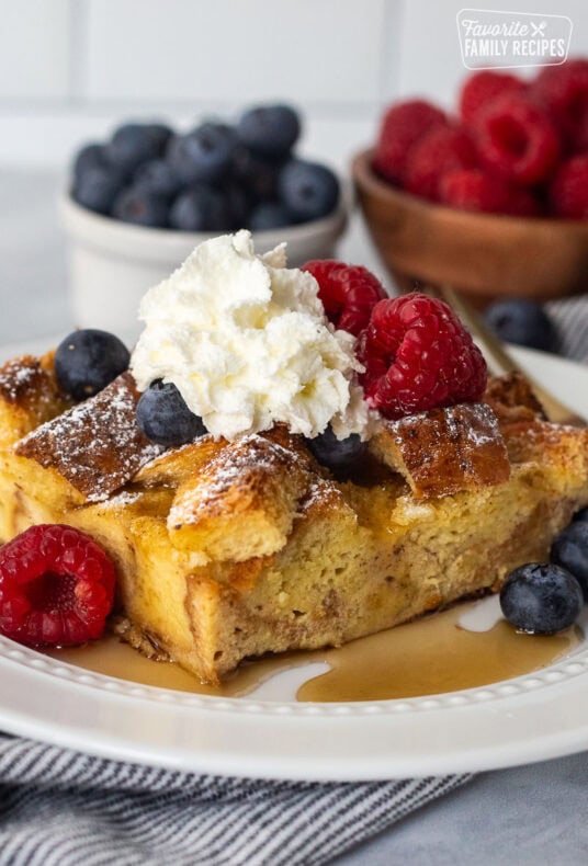 Plate with brioche French toast casserole, fresh blueberries, and raspberries and syrup.