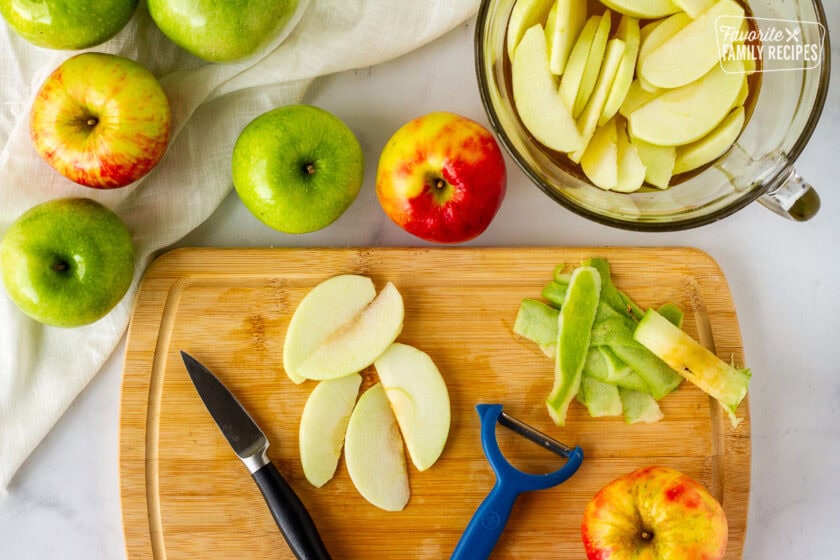 Apples peeling and slicing on a cutting board for Homemade Apple Pie filling.