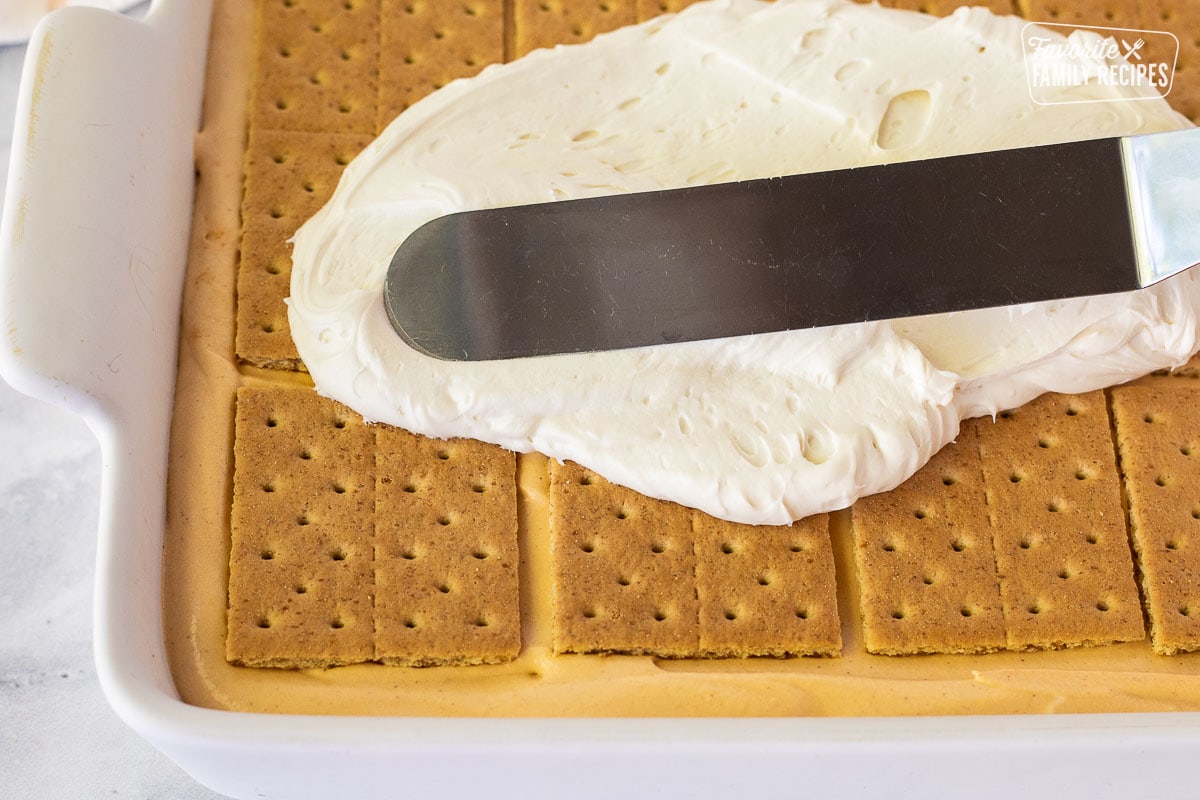 Spreading frosting on top of graham crackers for Pumpkin Eclair Cake.