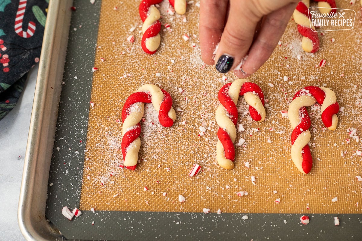 Sprinkling crushed candy, cane, and sugar on hot baked candy cane cookies.