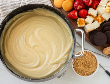 Cheesecake Fondue next to cutting board of cookies, cake and strawberries.