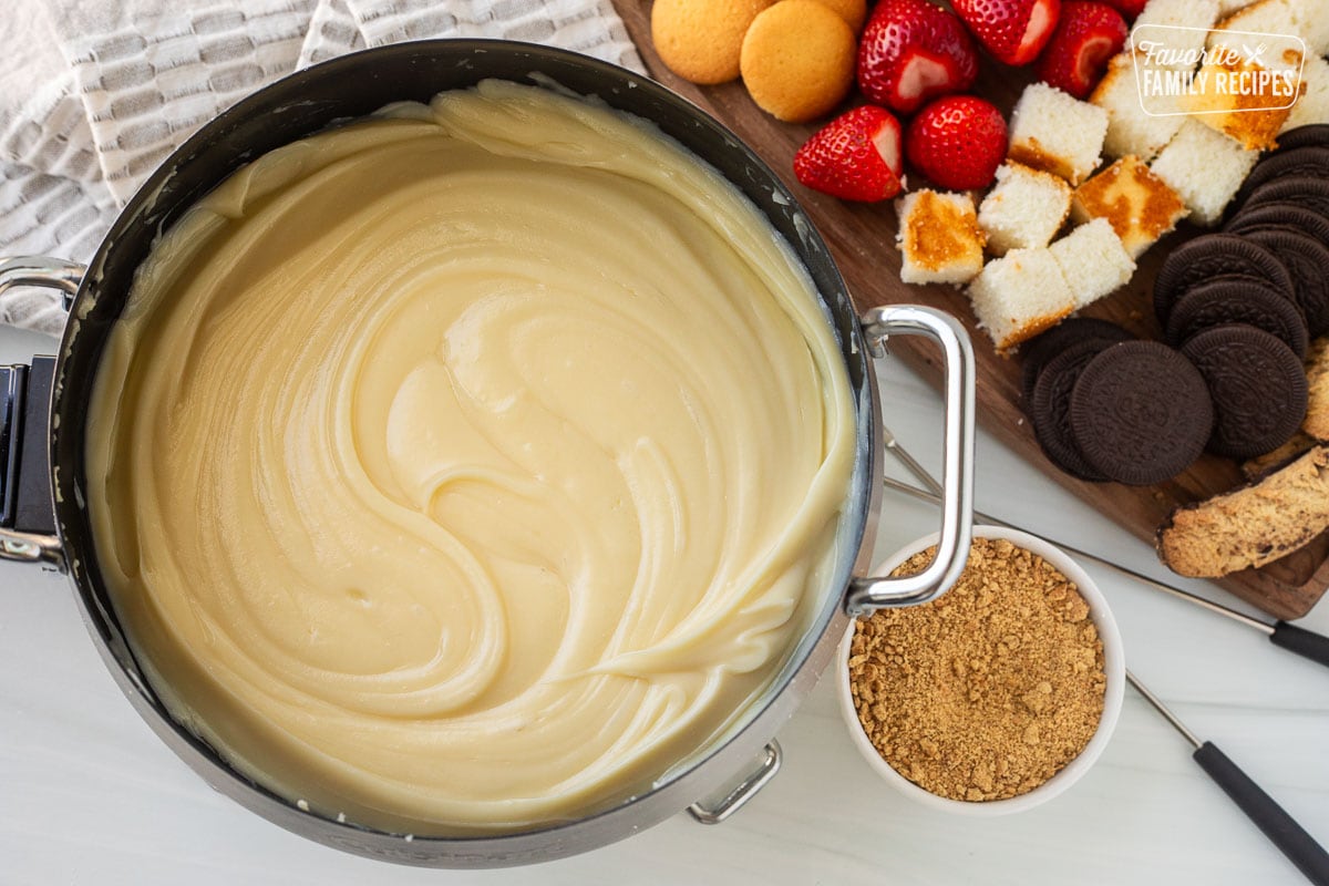 Cheesecake Fondue next to cutting board of cookies, cake and strawberries.