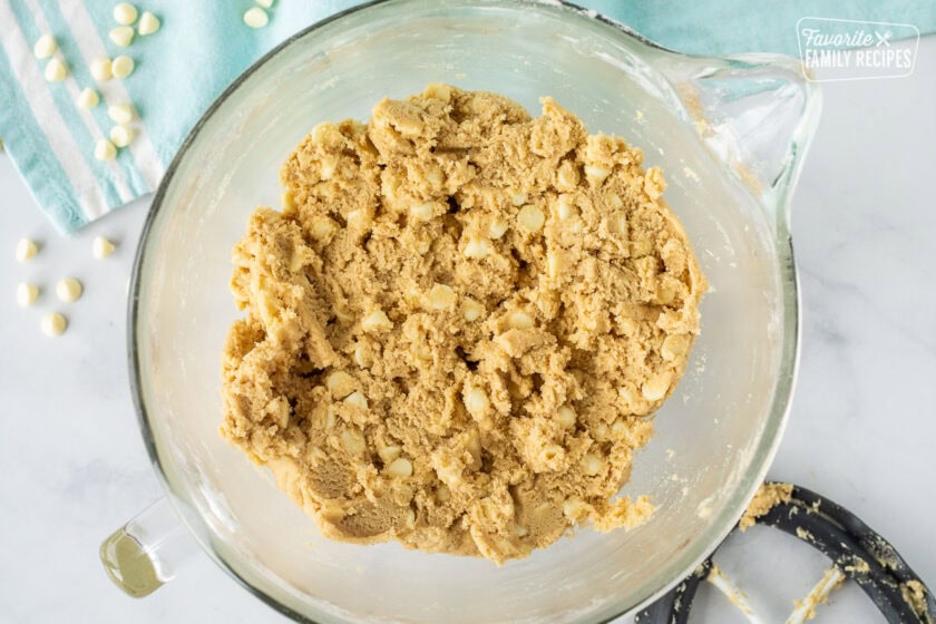 White chocolate chips added to vanilla cookie dough in a mixing bowl.