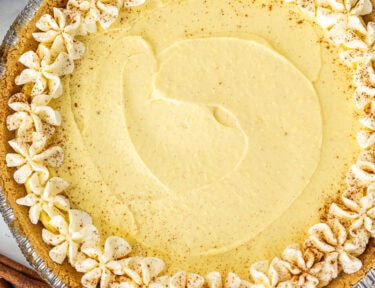 Whole egg nog pie decorated with piped, heavy cream and cinnamon.