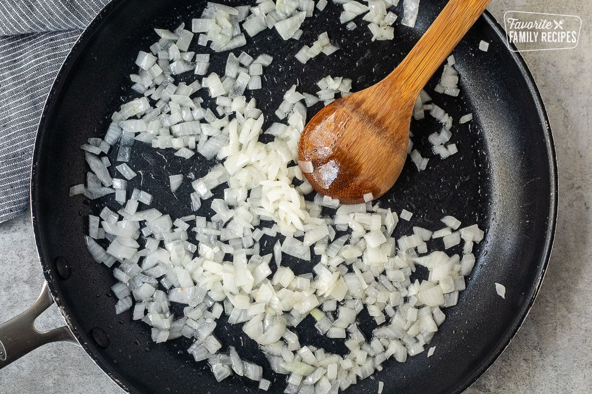 Skillet with cooked chopped onions, and a wooden spoon.